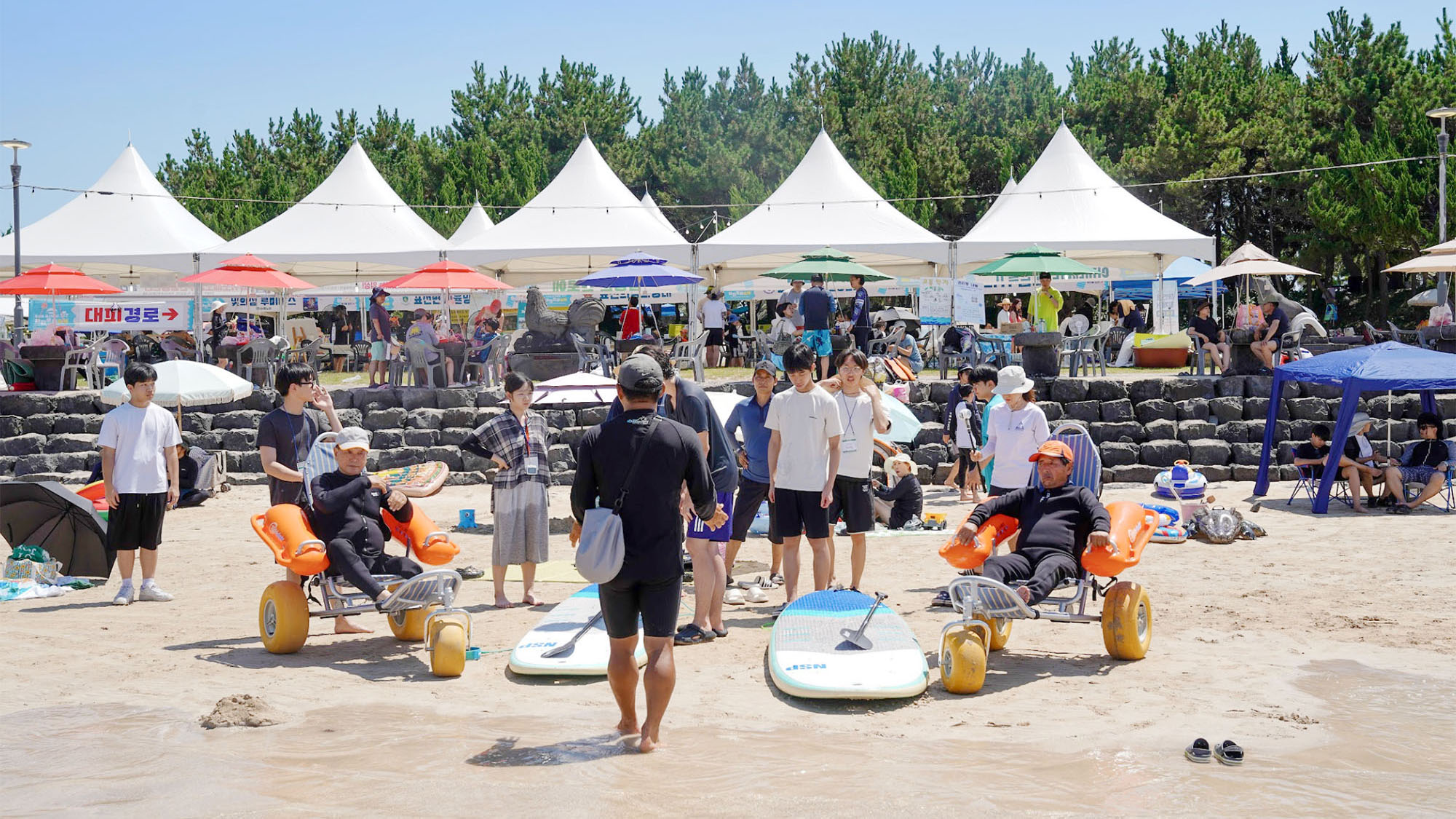 표선해수욕장 무장애 축제에서 패들보드 체험 안내를 받고 있는 참가자와 학생들. ⓒ이끼 동아리