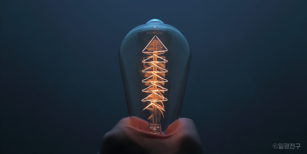 손으로 필라멘트가 보이는 전구를 잡고 있는 이미지예요.