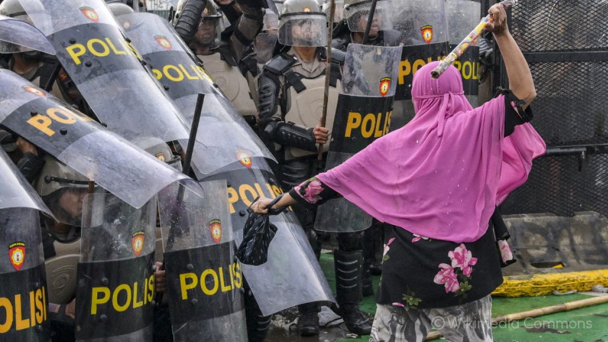 분홍색 히잡을 쓴 시위대 여성이 대나무 막대기를 들고 경찰에 맞서는 모습이에요.