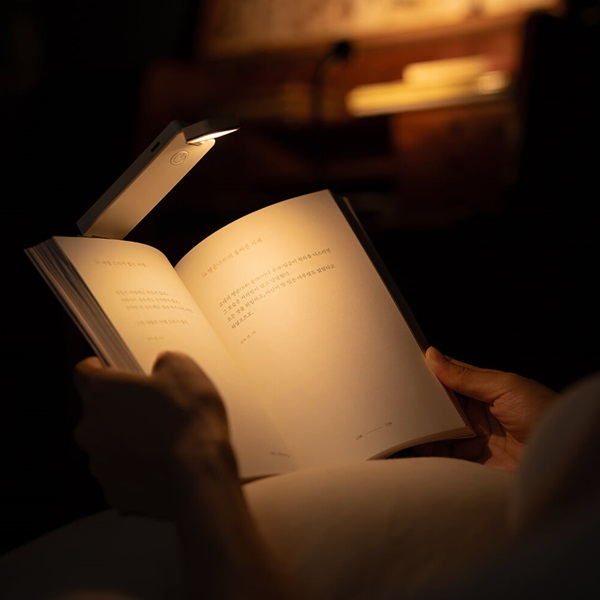 두 손으로 책을 펼치고 있는 모습. 책 상단에는 북라이트가 책갈피처럼 끼워져 있음.