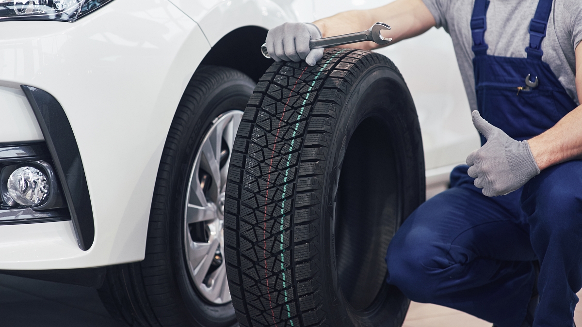 타이어 위에 손을 왼손을 올리고 무릎을 꿇고 있는 정비사가 왼손으로 엄지를 치켜 세운 모습이에요.